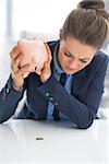 Closeup on business woman shaking out coin from piggy bank