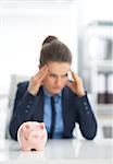 Closeup on piggy bank and stressed business woman in background