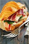 Croissant with ham and brie cheese on white parchment.