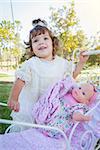 Adorable Young Baby Girl Playing with Her Baby Doll and Carriage Outdoors.