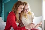 Two teenage girls looking at digital tablet in bedroom