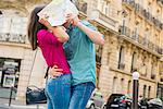 Young couple hiding behind map, Paris, France