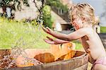 Female toddler splashing hands in water barrel