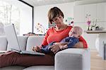 Mother and baby boy reclining on sofa with laptop