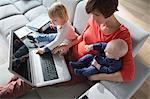 Mother, baby boy and female toddler using laptop on sofa