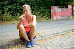 Young female runner sitting on sidewalk using cellphone