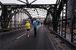 Two men running over city bridge