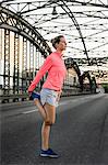 Young female runner stretching on bridge
