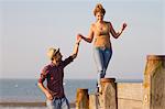 Young woman balancing on groynes holding man's hand