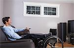 Man with spinal cord injury with leg in wheelchair watching TV with remote