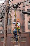 Cable lineman climbing up a ladder on city power pole