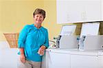 Senior woman standing in a laundry room against a commercial washing machine