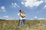 A couple standing in a field of wheat hugging.