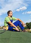 Roofer worker resting on top of building - sitting on bitumen roof shingles