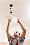 Electrician man screwing a new lightbulb into ceiling lamp - closeup