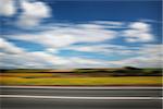 Road through the yellow sunflower field with clouds on blue sky motion blur