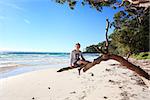 Teen boy sitting on a gum tree outstretched branch enjoying a vacation on a glorious day at the beach in NSW Australia
