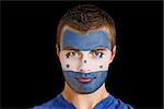 Composite image of serious young honduras fan with facepaint against black