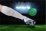 Composite image of close up of football player kicking brasil ball against football pitch under spotlights