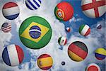 Footballs in various flag colours  against blue cloudy sky