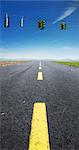 Close-up view of yellow, broken center line on deserted highway, with red traffic lights hanging on wires across road, Canada