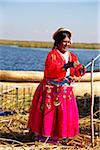 Woman in Peruvian clothing hanging up necklaces and traditional art on line outdoors, Floating Island of Uros, Lake Titicaca, Peru