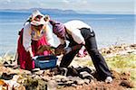 Man and woman in Peruvian clothing tending to earth covered barbeque, Taquile Island, Lake Titicaca, Peru