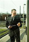 Businessman holding tablet computer and looking at cell phome, standing at train station outdoors, Mannheim, Germany