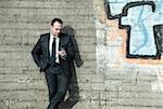 Businessman standing next to stone wall outdoors, looking at cell phone, Germany