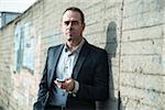 Portrait of businessman standing next to stone wall outdoors, holding cell phone, Germany