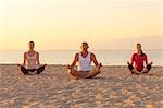 People practising yoga on beach, lotus pose