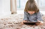 Boy using digital tablet while lying on rug at home