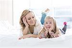 Mother looking at cute daughter making faces while lying in bed
