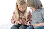 Brother and sister using tablet PC in bedroom
