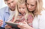 Mid adult parents using tablet PC with daughter at home