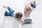 High angle view of brother and sister using laptop on floor at home