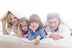 Portrait of happy parents and children lying under bed cover