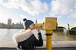 Side view of young woman looking through telescope by river Thames, London, UK