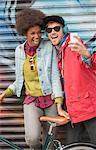 Couple taking self-portrait with cell phone against graffiti wall