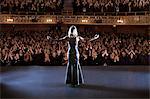 Performer standing with arms outstretched on stage in theater