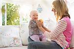 Mother playing with baby girl on sofa