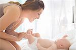 Mother playing with baby girl on bed