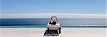 Woman relaxing on lounge chair at poolside overlooking ocean