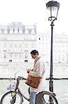 Businessman using cell phone on bicycle along Seine River, Paris, France