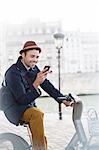 Businessman using cell phone on bicycle along Seine River, Paris, France