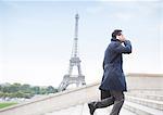 Businessman talking on cell phone and ascending steps near Eiffel Tower, Paris, France
