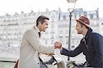 Businessmen shaking hands on bicycles along Seine River, Paris, France
