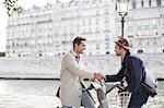 Businessmen handshaking on bicycles along Seine River, Paris, France