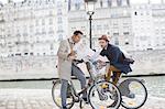 Men on bicycles reading map along Seine River, Paris, France