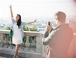 Man photographing girlfriend with city in background